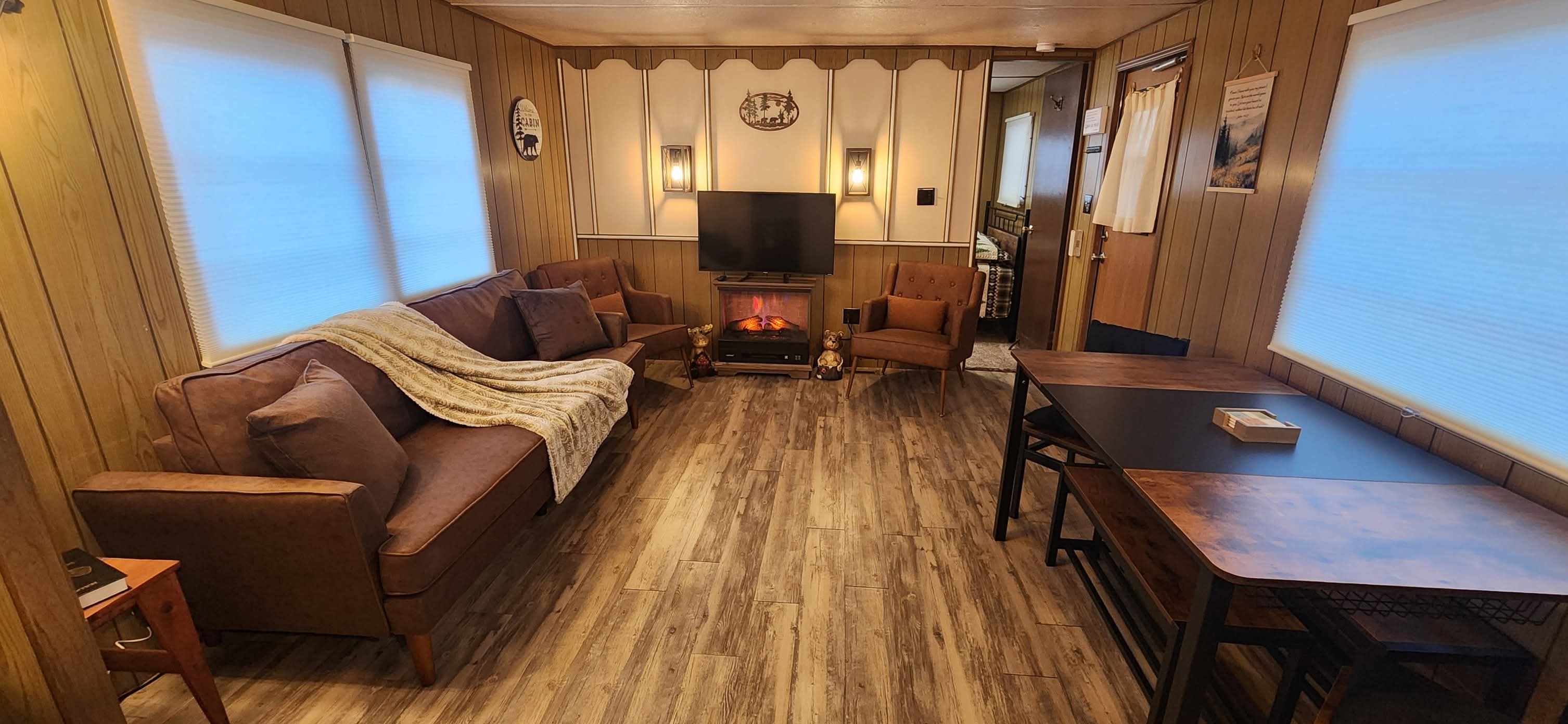 Warm and inviting living room featuring comfortable seating arranged facing a TV, rustic wood accents, and views into the kitchen and dining area beyond, creating an open floor plan ideal for relaxation